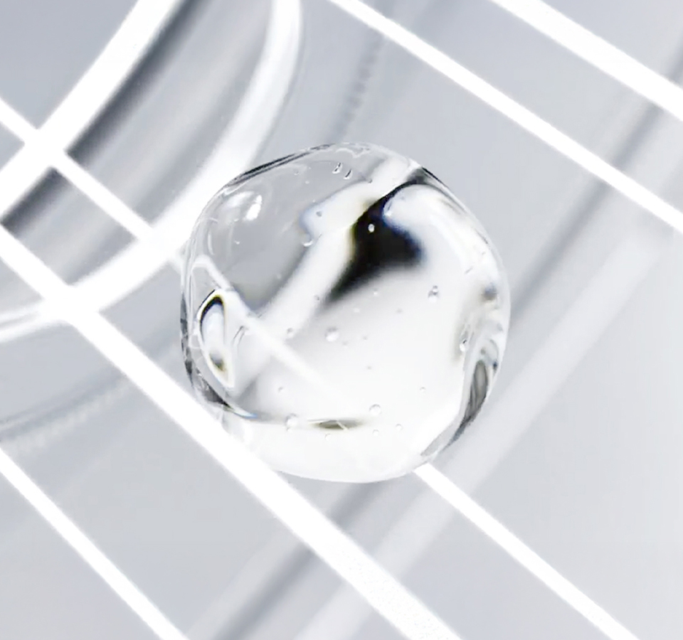 엠디 리쥬브네이팅 부스터 샷 엠디 세럼의 촉촉하고 투명한 제형이 빛을 받아 반짝이는 모습으로, 피부에 수분과 탄력을 더하는 세럼의 효과를 시각적으로 보여줍니다.